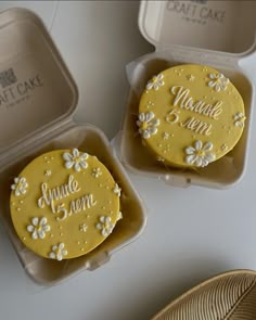 two yellow decorated cakes sitting in plastic containers