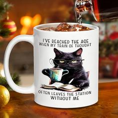 a black cat is drinking out of a mug