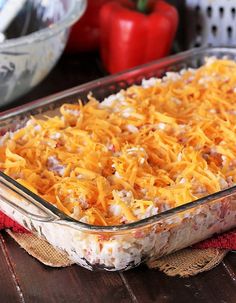 a casserole dish with cheese and meat in it on a wooden table next to red peppers