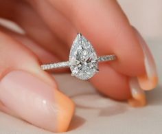 a woman's hand holding an engagement ring with a pear shaped diamond on it