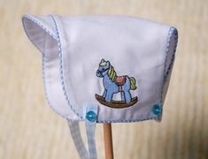 a blue and white hat with a horse embroidered on the front, sitting on top of a wooden stick