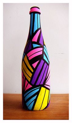 a colorful painted vase sitting on top of a wooden table next to a white wall