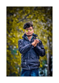 a man wearing glasses standing in front of some trees and looking at his cell phone