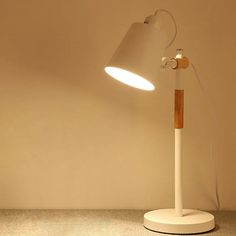 a white table lamp with a wooden stick on the base in front of a beige wall