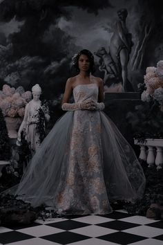 a woman in a wedding dress standing on a checkered floor with statues behind her