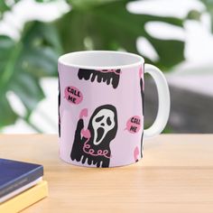 a pink coffee mug with a black and white image of a ghost on it sitting on a table