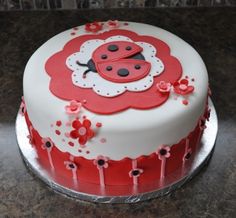 a red and white cake with a ladybug decoration on the top is sitting on a table