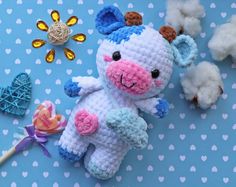 a crocheted cow laying next to cotton balls and a pinwheel on a blue background