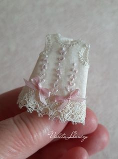 a hand holding a miniature white sweater with pink bows