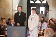 two men standing at podiums in front of a group of people, one wearing a suit and tie