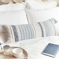 a white bed topped with lots of pillows next to a tray filled with cups and saucers