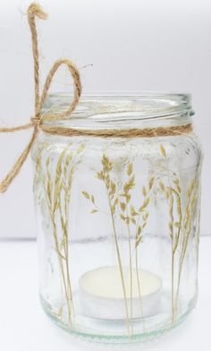 a glass jar filled with water and some dried grass on top of the inside is a candle