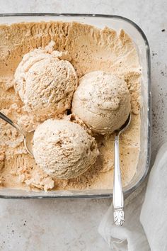 three scoops of ice cream in a glass dish with a spoon on the side