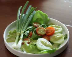 a white bowl filled with lettuce, tomatoes and cucumbers on top of a wooden table