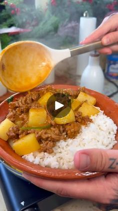 a person is spooning some food out of a bowl with rice on the side