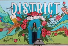 a woman standing in front of a mural on the side of a building with flowers