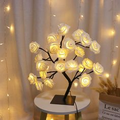 a lighted tree with white roses sitting on top of a table