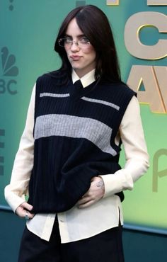 a woman with glasses standing in front of a green wall wearing a black and white sweater