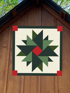 a quilt hanging on the side of a wooden building with trees in the back ground