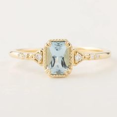 a gold ring with an aqua blue topazte and diamonds on the sides, in front of a white background