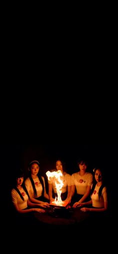 a group of women sitting around a fire pit in the dark with their backs turned