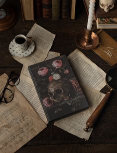 an open book sitting on top of a wooden table next to glasses and a candle