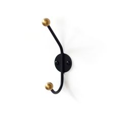 a black and gold hook on a white wall with two brass balls in the middle