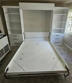 an empty bed frame in a room with built - in bookcases and drawers