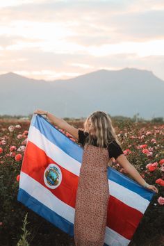 a woman holding a flag in a field of flowers with mountains in the back ground