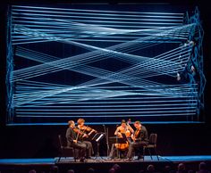 three men sitting on stage playing instruments in front of a large screen with lines drawn across it