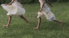 two women in white dresses are running through the grass