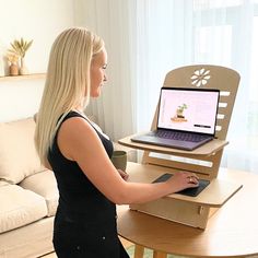 a woman standing in front of a laptop computer on a wooden table with a stand