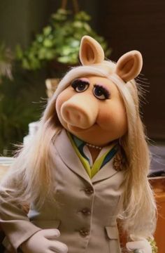 the miss piggy doll has long blonde hair and is wearing a white suit with yellow stripes