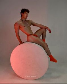 a naked man sitting on top of a round object with his legs crossed and no shirt on