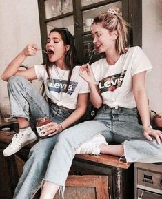 two young women sitting on top of a wooden table