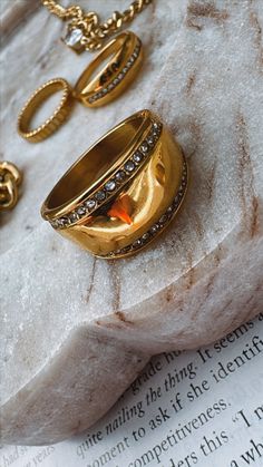 two gold rings sitting on top of an open book next to a chain and ring