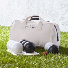 a white bag sitting on top of a green field next to bowling balls and racquets