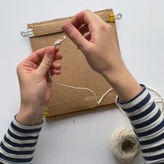 two hands are holding yarn and thread in front of a piece of cardboard