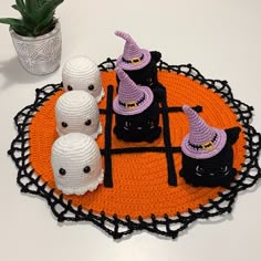 crocheted halloween decorations with black cats and witches on an orange doily next to a succulent plant