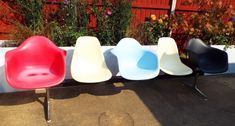 four different colored chairs sitting next to each other in front of a red fence and flowers