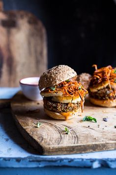 three burgers sitting on top of a wooden cutting board