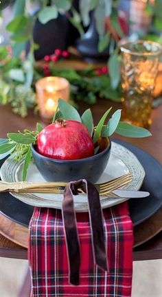 an apple in a bowl sitting on a table with greenery and candles behind it