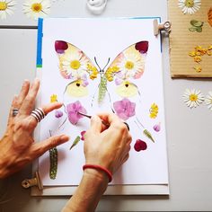 a person is making a butterfly card with flowers and butterflies on the paper next to it