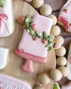 decorated cookies and pastries on a wooden tray with pink icing, flowers and leaves