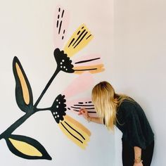 a woman standing next to a wall with flowers painted on it