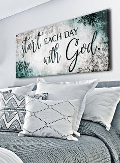 a bed topped with pillows next to a painting on the wall above it that says start each day with god