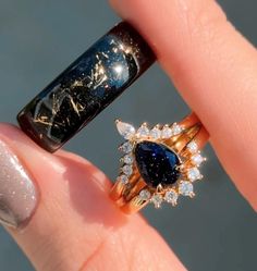 a close up of a person's hand holding a ring with a blue and white diamond