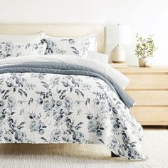 a bed with blue and white floral comforter on top of it in a bedroom