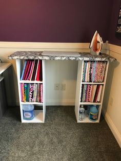 an ironing board sitting on top of a white desk next to a book shelf