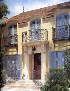 a large yellow house with blue shutters and iron balconies on the second story